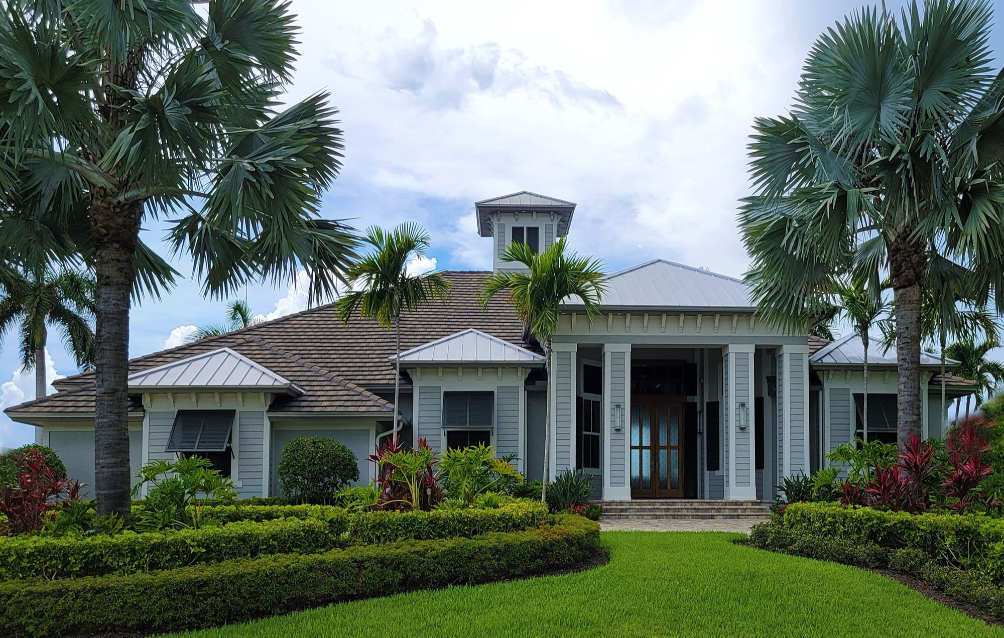 White house with a metal roof, cupola and columned entrance behind clipped hedges
